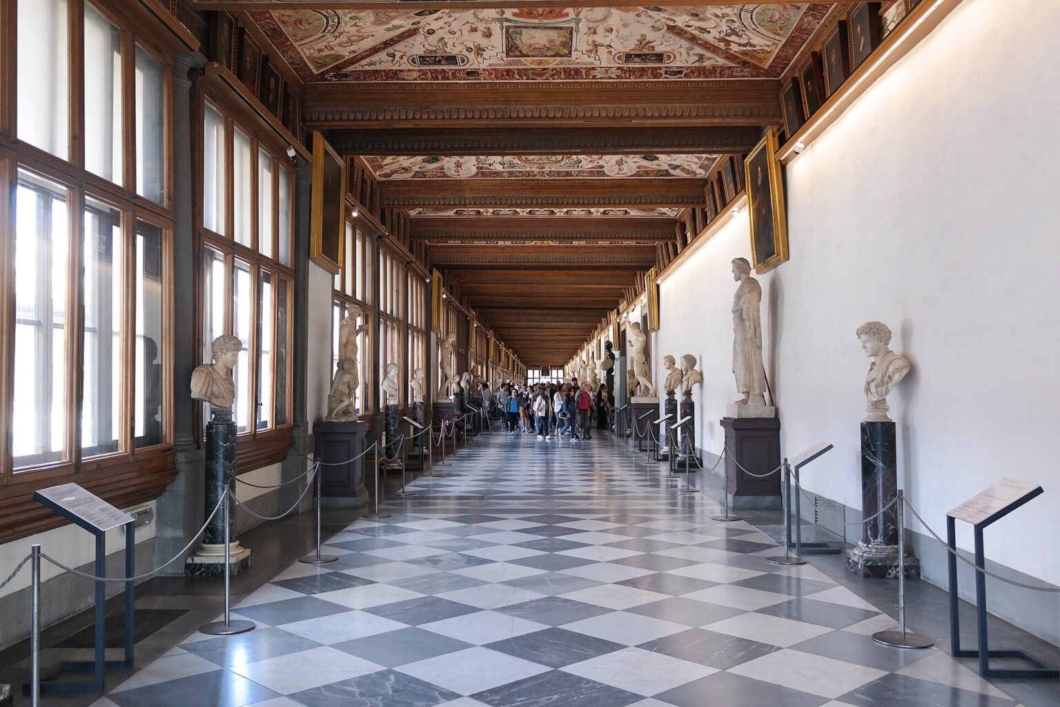 Corridoio del livello superiore della Galleria degli Uffizi con statue e visitatori